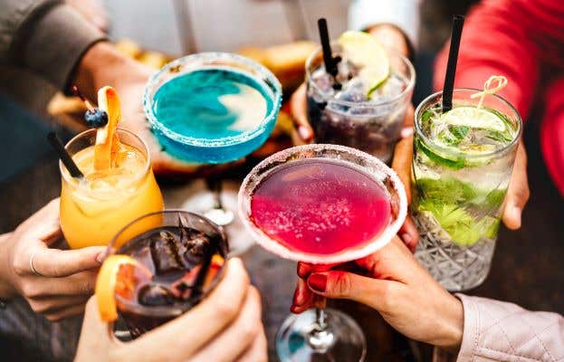 several colorful cocktails raised in cheers