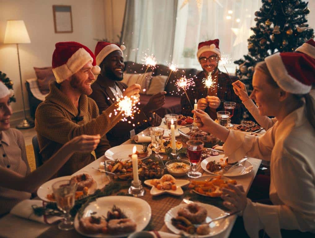 Multi-ethnic group of people holding sparklers while enjoying Christmas dinner at home with Christmas foods