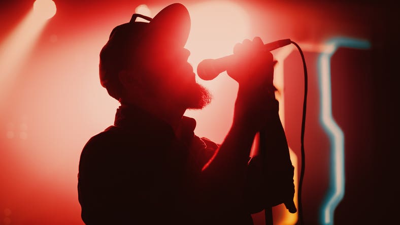 Rock Band Performing at a Concert in a Night Club. Portrait of a Lead Singer Singing into Microphone. Live Music Party in Front of Bright Colorful Strobing Lights on Stage. Fun Happenings In SWFL This Weekend