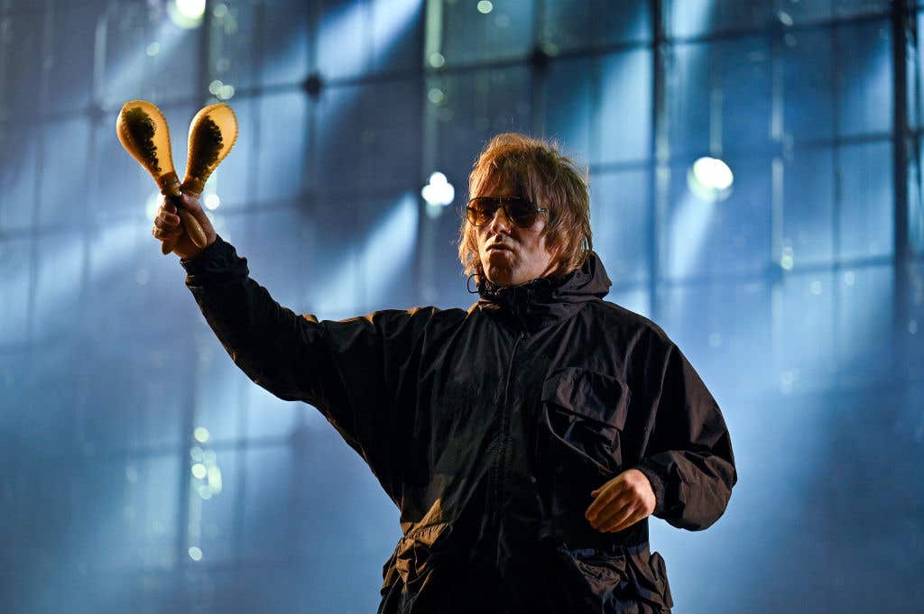 Liam Gallagher performing on stage wearing a parka and sunglasses