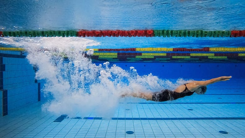 Female swimmer in water immersion phase, entering and sliding below the water surface making wonderful bubbles, underwater shot.