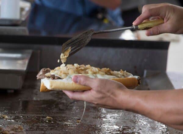 Person making a Philly Cheesesteak. University Of Miami Baseball Stadium Unveils Cheesesteak Milkshake