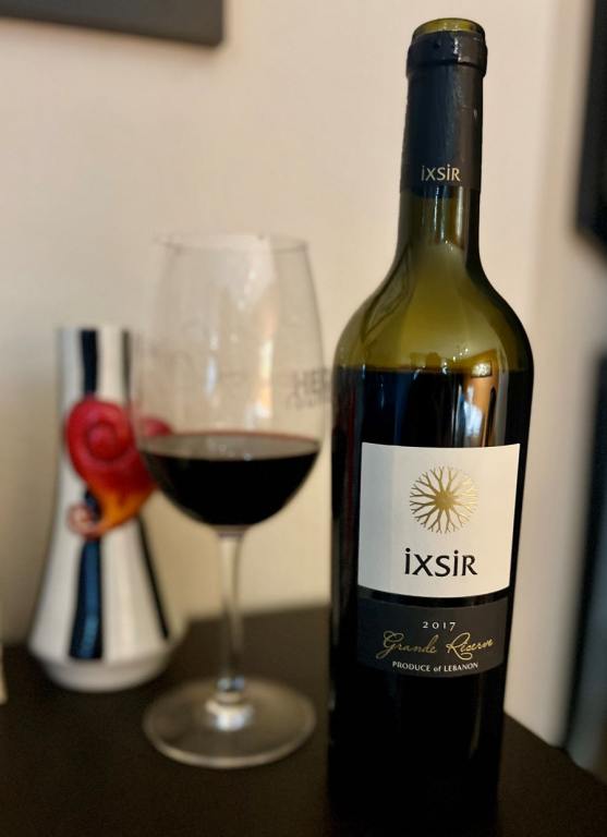 Wine bottle with a glass of red wine and a black and white vase in the background