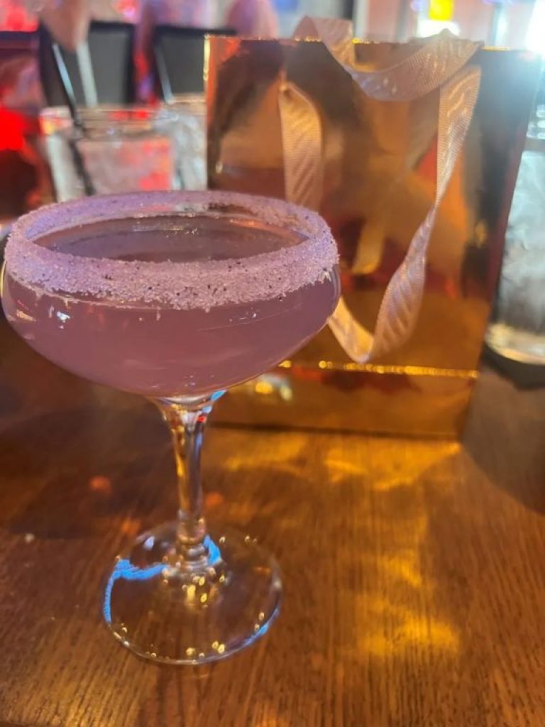 Purple cocktail in a coupe with a sugared rim for Sizzle Dining stop at Stones Throw