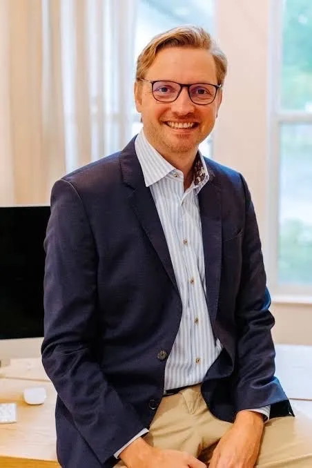 Man in a suit sitting on a desk and smiling as Innovations For Florida Attractions Are Out This Week